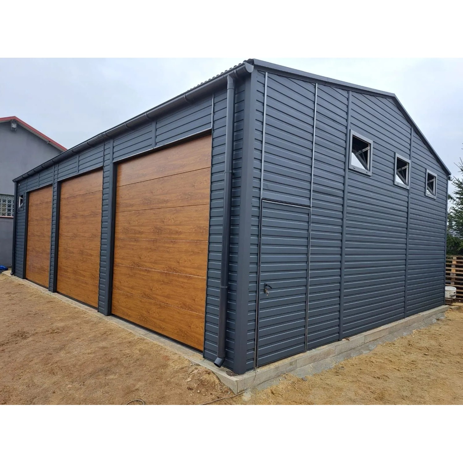 Große Liderstal Fertiggarage aus graphitfarbenem Trapezblech mit drei Sektionaltoren in Goldene Eiche Optik.