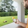 Mann steuert Stiga Mähroboter G 600 per App auf dem Smartphone im Garten.