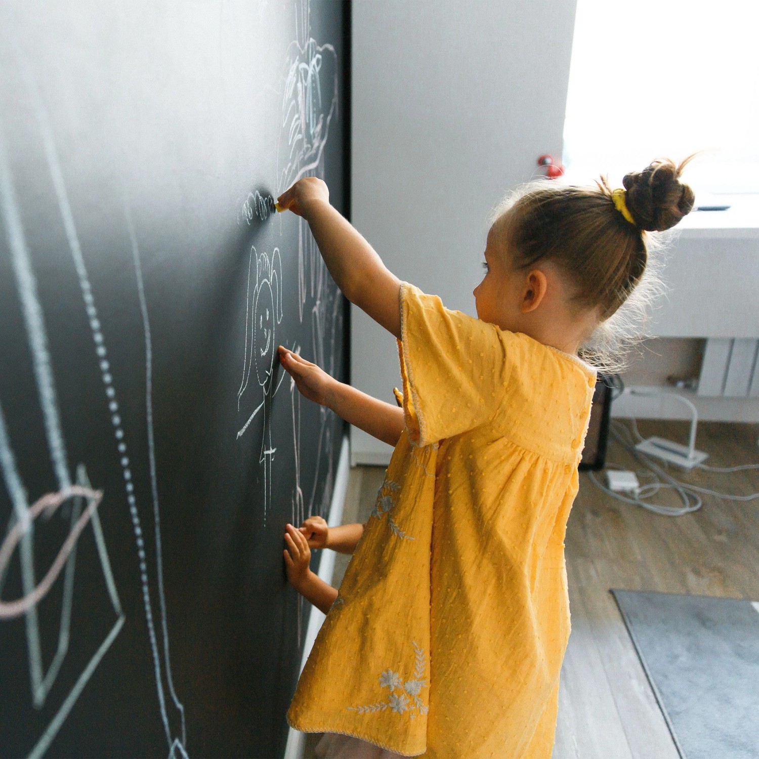Kind malt mit Kreide auf schwarzer, selbstklebender Tafelfolie an der Wand. Ideal für Kinderzimmer.