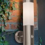 Moderne LED-Außenwandleuchte Bultei aus Edelstahl mit Bewegungsmelder an einer Backsteinwand.
