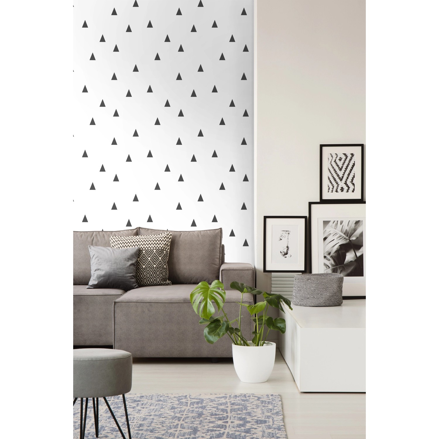 Wohnraum mit Walls4You Tapete Dreiecke Schwarz-Weiß an der Wand hinter einem grauen Sofa.
