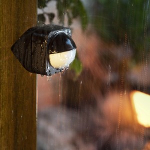 Philips Hue Outdoor Bewegungsmelder, dunkel, wetterfest im Regen an Holzpfosten. Für smarte Lichtsteuerung im Außenbereich.