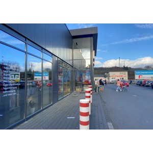 Weiß-rote Schake Absperrpoller (Ø 323 mm) vor einem Gebäude. Baugeräte zur Flächenabsperrung.