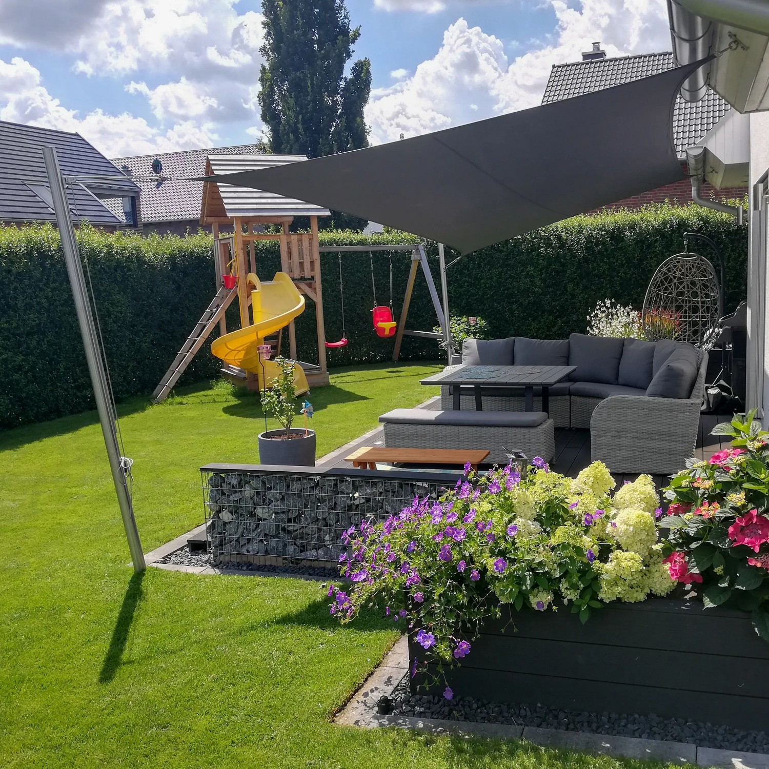 Anthrazitfarbenes Toldoro Sonnensegel Komplettset im Garten mit Möbeln und Spielplatz.