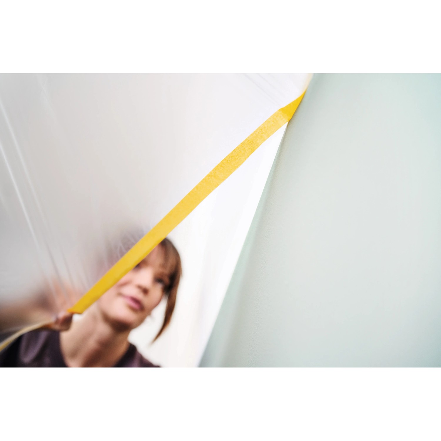 Frau bringt Tesa Abdeckfolie mit Klebeband Easy Cover Perfect+ an Wand an.