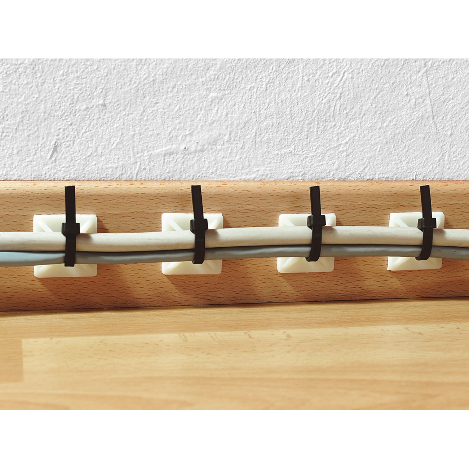 Weisse Klebesockel 19x19 mm mit Kabelbindern fixieren Kabel an einer Holzleiste.
