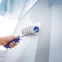 Hand streicht weiße Wand mit LUX Dispersionswalze 18 cm Polymix Gold-Grau-Gestreift.
