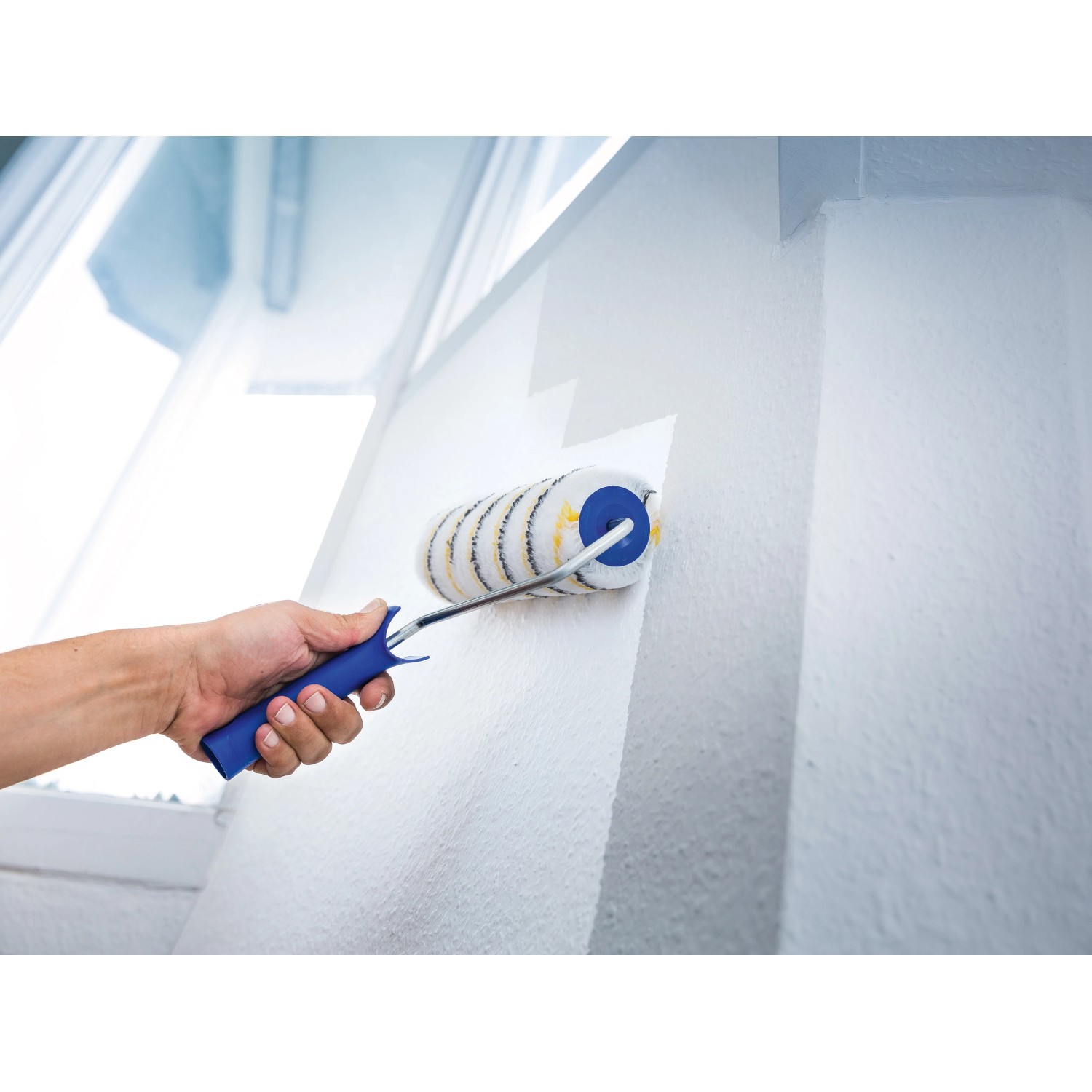 Hand streicht weiße Wand mit LUX Dispersionswalze 18 cm Polymix Gold-Grau-Gestreift.
