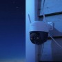 IMOU Cruiser 2C WLAN Überwachungskamera, weiß-grau, an Holzwand bei Nacht. Schwenk- & Neigefunktion, Nachtsicht.