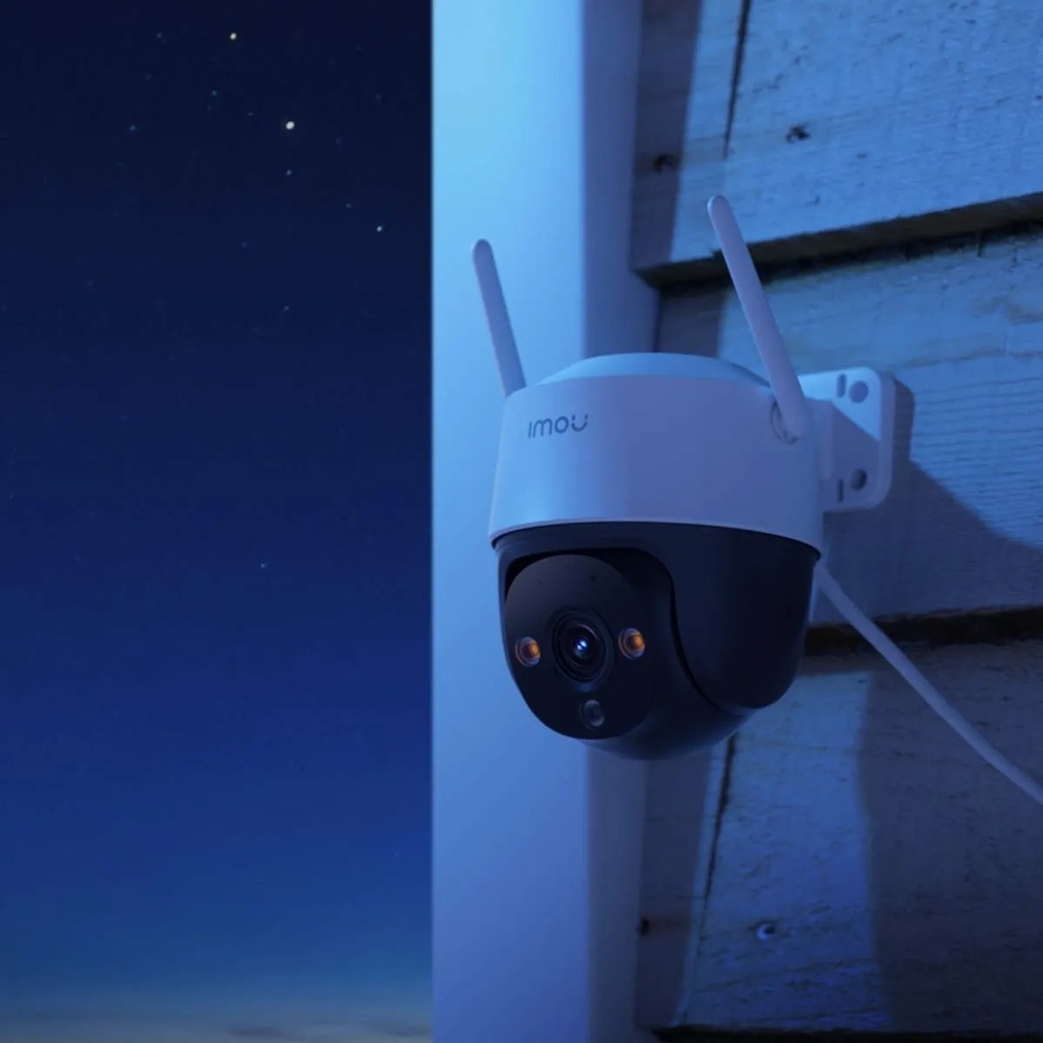 IMOU Cruiser 2C WLAN Überwachungskamera, weiß-grau, an Holzwand bei Nacht. Schwenk- & Neigefunktion, Nachtsicht.