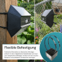 Schwarze LUXULA Solar Wandleuchte mit Bewegungsmelder, befestigt mit Kabelbindern an Zaun und Holzpfosten.