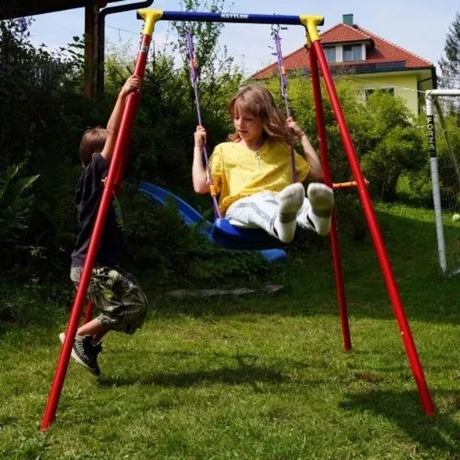 Kettler Einzelschaukel Single in Rot/Blau mit Kind beim Schaukeln im Garten.