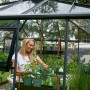 Frau im anthrazitfarbenen Juliana Gewächshaus Oase 13 mit Pflanzen auf Regalen.