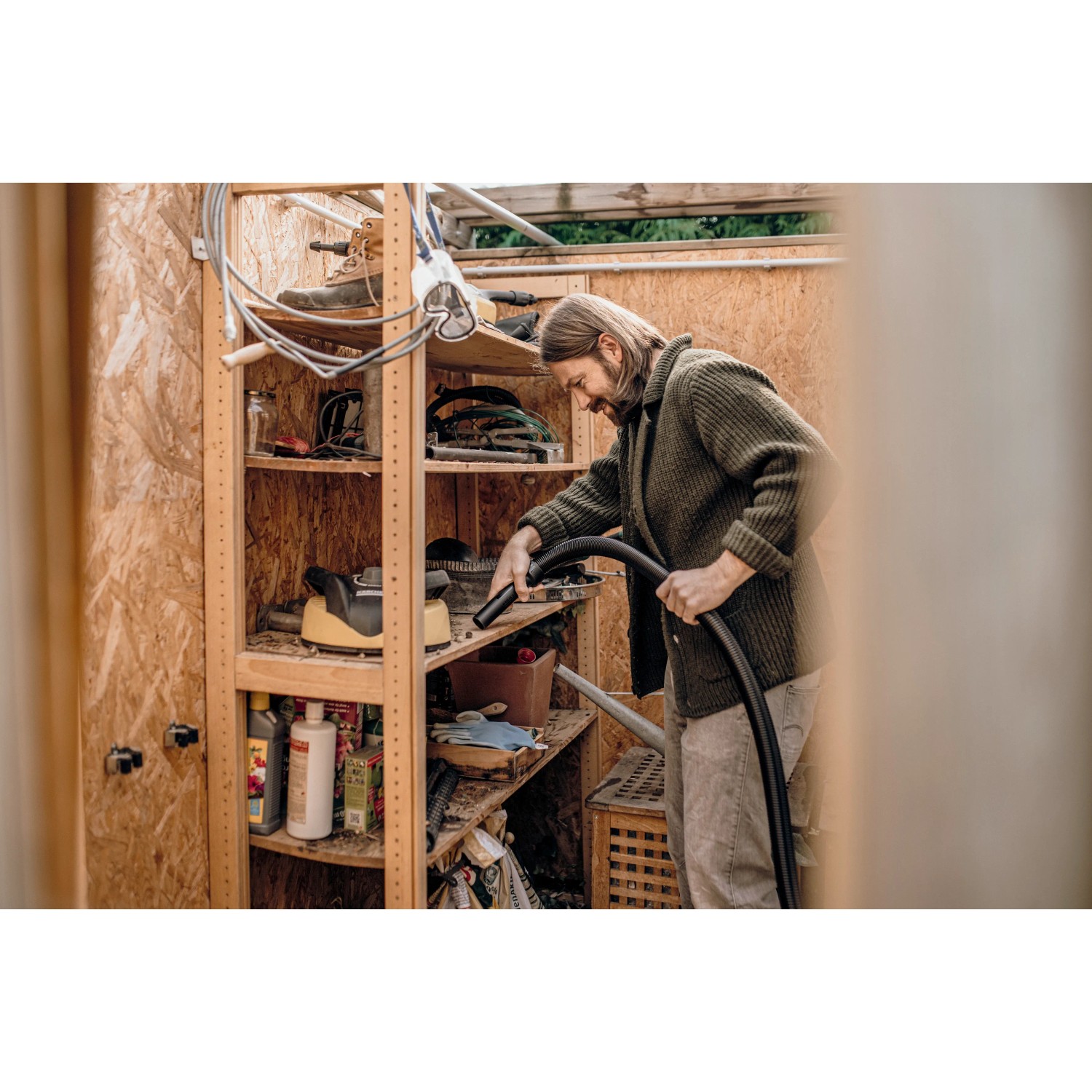 Mann saugt mit Kärcher WD 1 Classic Nass-Trockensauger Regal in Werkstatt ab.