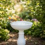 Weiße Polyresin Vogeltränke auf Säule im Garten, ein Rotkehlchen trinkt Wasser. Antikes Vogelbad für Wildvögel.