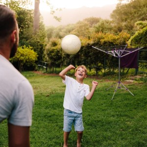 Junge spielt mit Ball im Garten, im Hintergrund eine lila Relaxdays Wäschespinne.