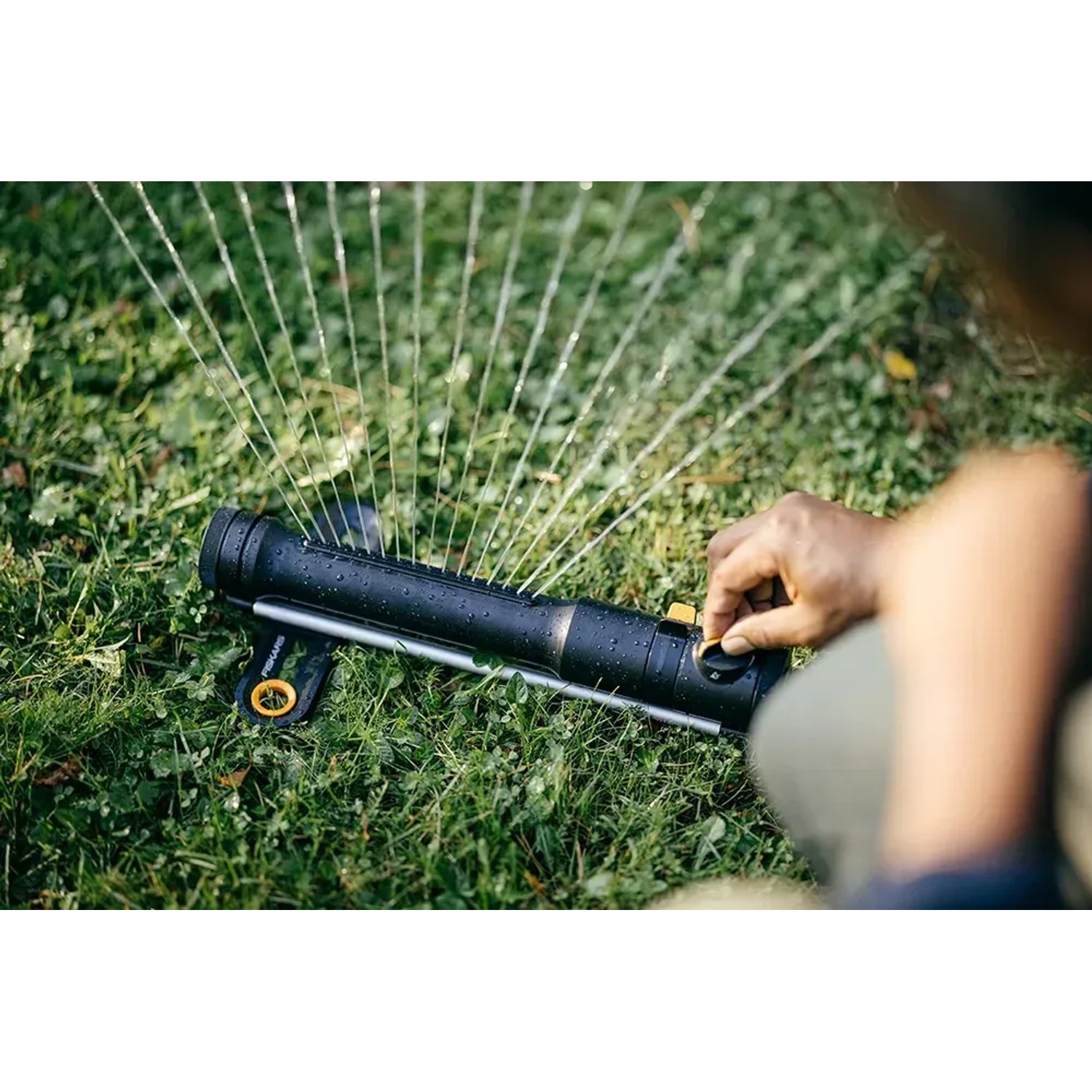 Fiskars Comfort S-M oszillierender Regner in Schwarz-Orange im Einsatz auf Rasen.