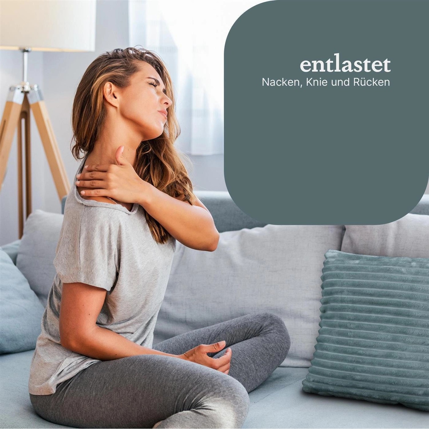 Frau mit Nackenschmerzen sitzt auf Sofa mit graugrünem Bestlivings Sofakissen Cord Optik 40x40cm.