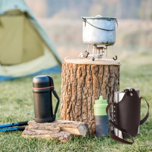 Großer silberner Edelstahl Flachmann mit brauner Kunstlederhalterung im Outdoor-Camping-Setting.