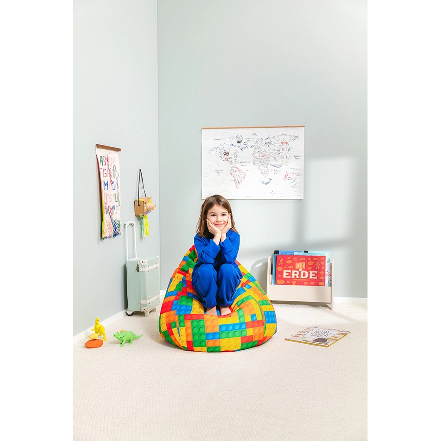 Mädchen sitzt auf buntem Sitting Point Sitzsack Bricks (120 l) im Kinderzimmer.