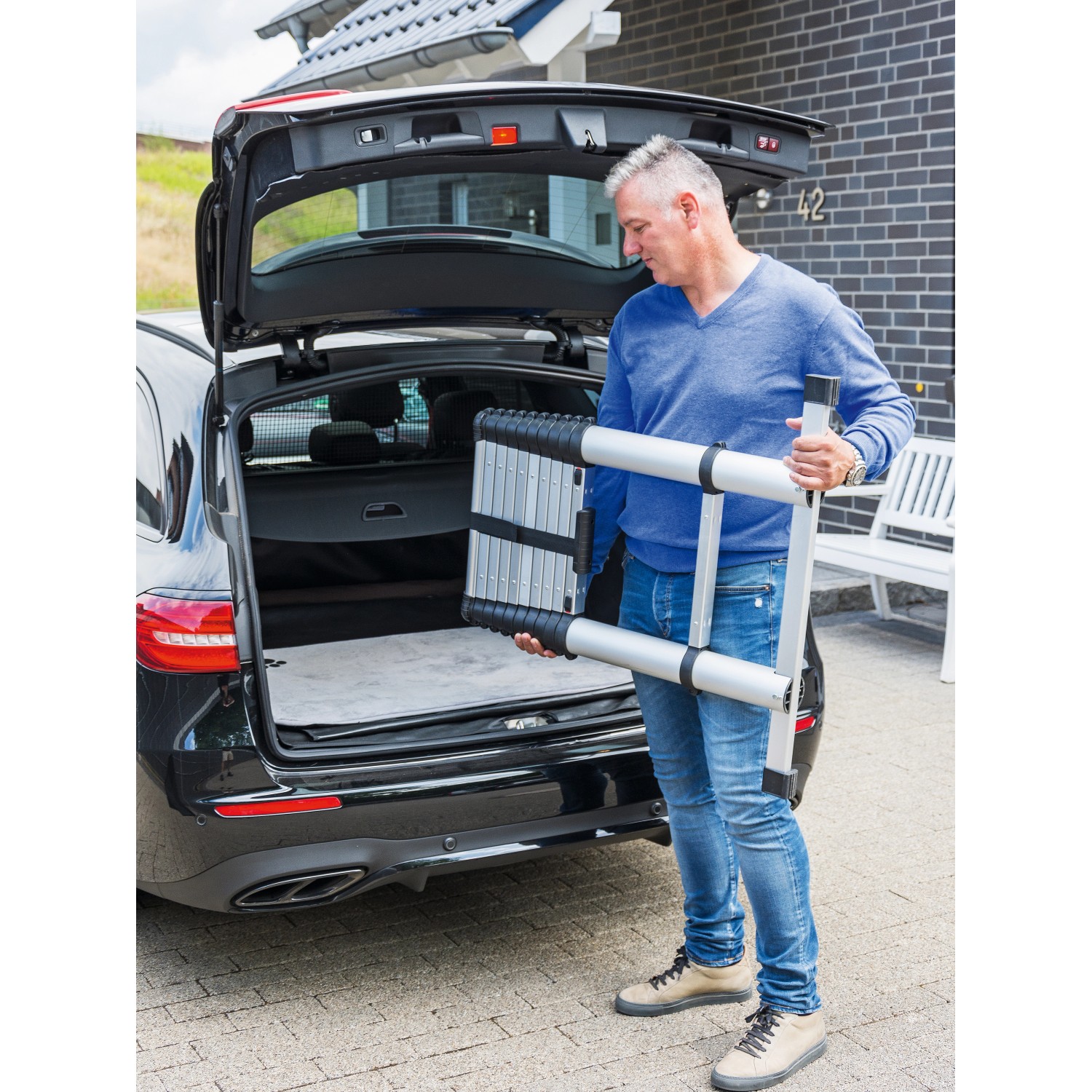 Zusammengeklappte Aluminium Teleskopleiter (11-stufig) wird aus einem Kofferraum gehoben.