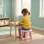 Rosa Kindersitzhocker aus Kunststoff. Ein Kind sitzt sicher auf dem stabilen Hocker am Tisch im Kinderzimmer. Kippsicher.