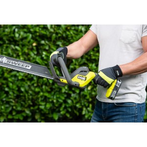 Ryobi Akku-Heckenschere RY18HT55A-120 mit Akku und Ladegerät im Einsatz, vor grüner Hecke.