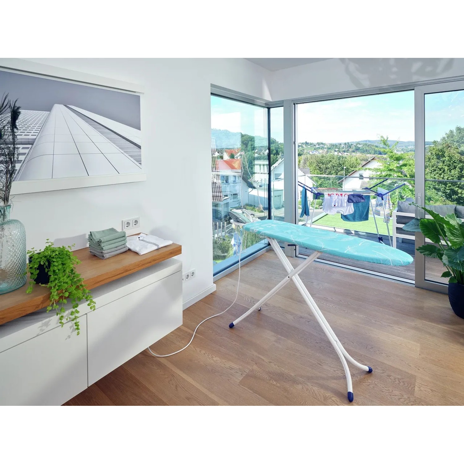Leifheit Bügeltisch AirBoard Compact M Plus mit blauem Bezug und Bügeleisenablage im Raum.