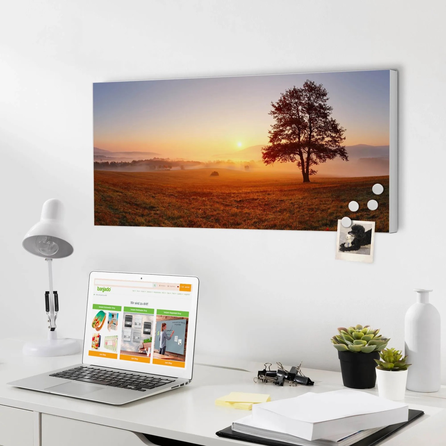 Banjado Magnettafel mit Sonnenaufgang-Motiv, weißen Magneten, an weißer Wand über Schreibtisch mit Laptop.