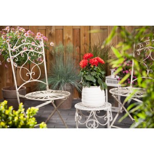 Orange Dahlie 'Dahlietta Rachel' im Topf auf Gartentisch, umgeben von Gartenmöbeln.