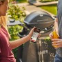 Weber Connect Grillthermometer in Nutzung mit Smartphone App und Grill im Hintergrund.