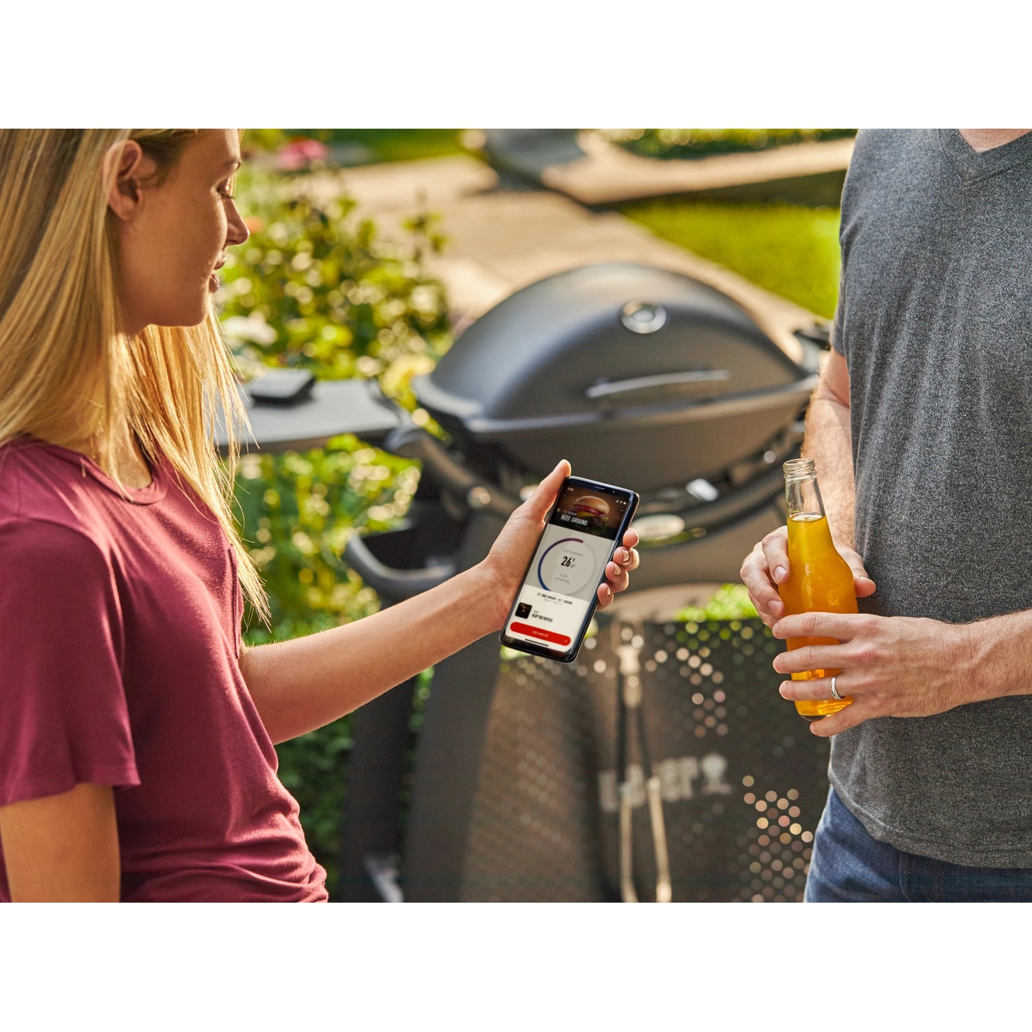 Weber Connect Grillthermometer in Nutzung mit Smartphone App und Grill im Hintergrund.