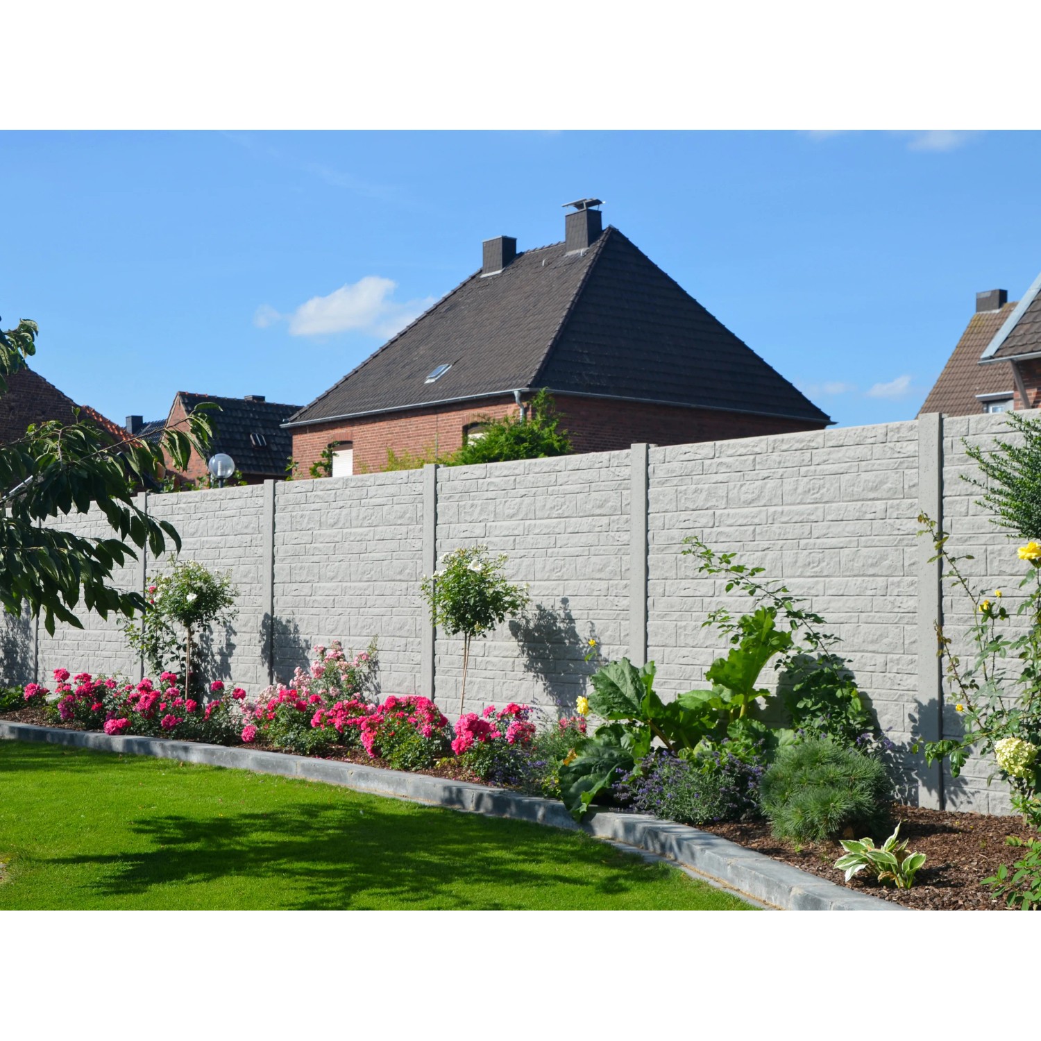 Graue Betonzaun-Platte Fels (200x38,5x3 cm) als Sichtschutz im Garten mit Blumen und Rasen.