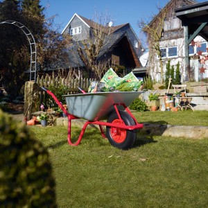 Verzinkte Pro-Bau-Tec Einrad-Schubkarre mit rotem Gestell und 85 l Mulde im Garten.