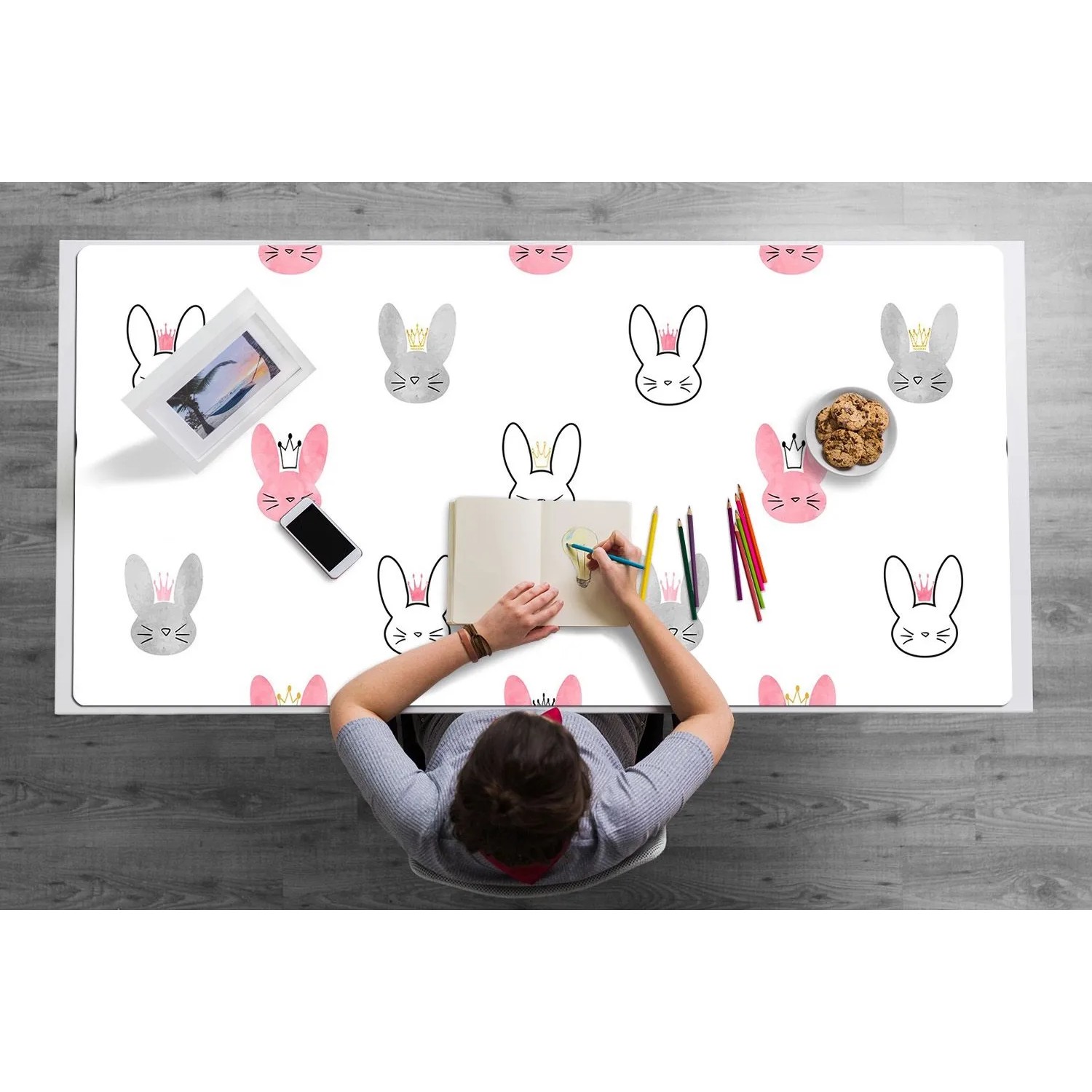 Weiße PVC Schreibtischunterlage mit rosa und grauen Kaninchenköpfen und Kronen. Eine Person zeichnet darauf. Perfekt für Büro & Kinderzimmer.