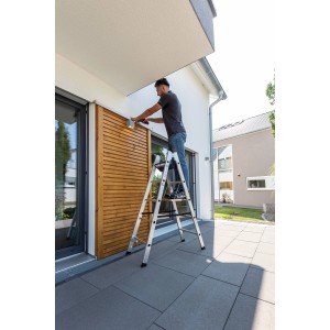 PROREGAL Sprossen-Stehleiter (2x5) im Einsatz: Mann montiert Lampe an Hauswand. Leiter aus Aluminium.