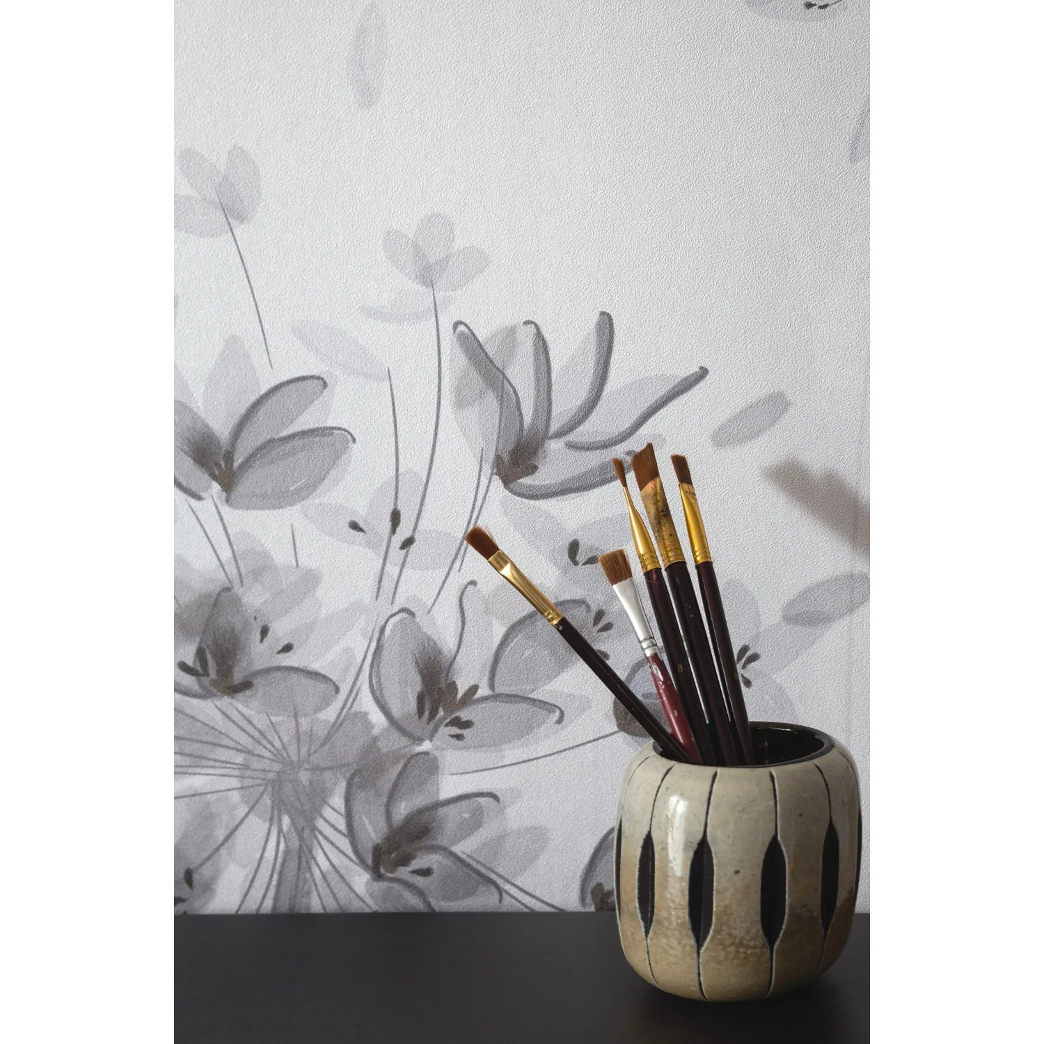 Schöner Wohnen Fototapete Floral Grau-Beige mit Pinsel im Topf vor der Tapete.