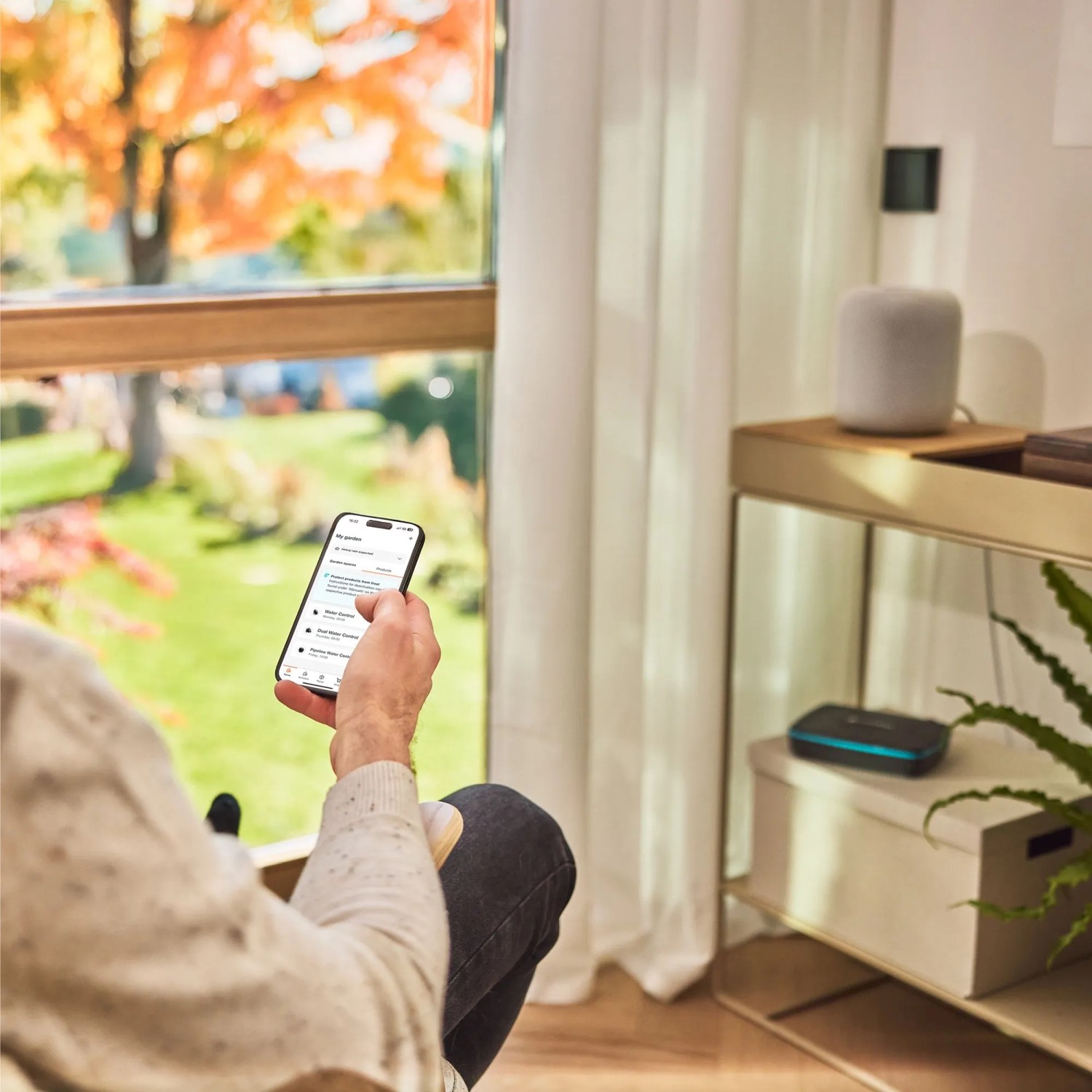 Mann steuert Gardena Smart Pipeline Water Control per App im Wohnzimmer.