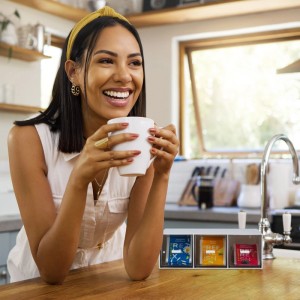 Frau mit Teetasse neben Relaxdays Tee Organizer mit 3 Fächern, weiß/transparent.