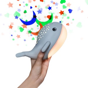 Graues LED-Nachtlicht Willy Whale mit Sternprojektor in Hand, projiziert Sterne und Monde.