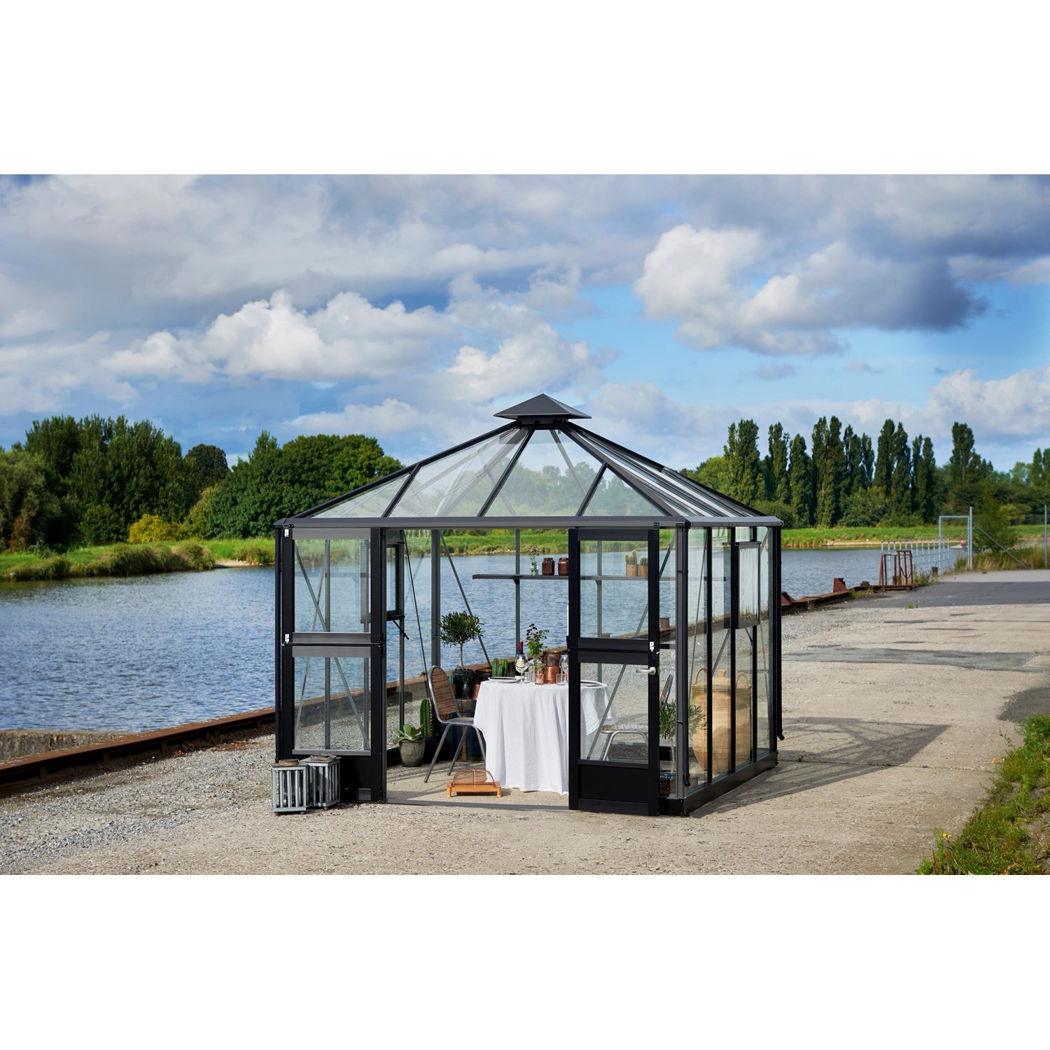 Juliana Gewächshaus Oase 8 Anthrazit mit Tisch und Stuhl am Wasser.