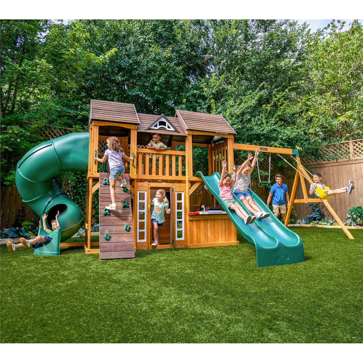 Zwerkules Spielturm Bolzo mit Rutschen, Schaukel und Kletterwand im Garten mit spielenden Kindern.