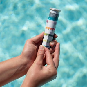 Bayrol QuickTest 50 Pool Teststreifen zur Wasseranalyse in der Hand vor Poolwasser.