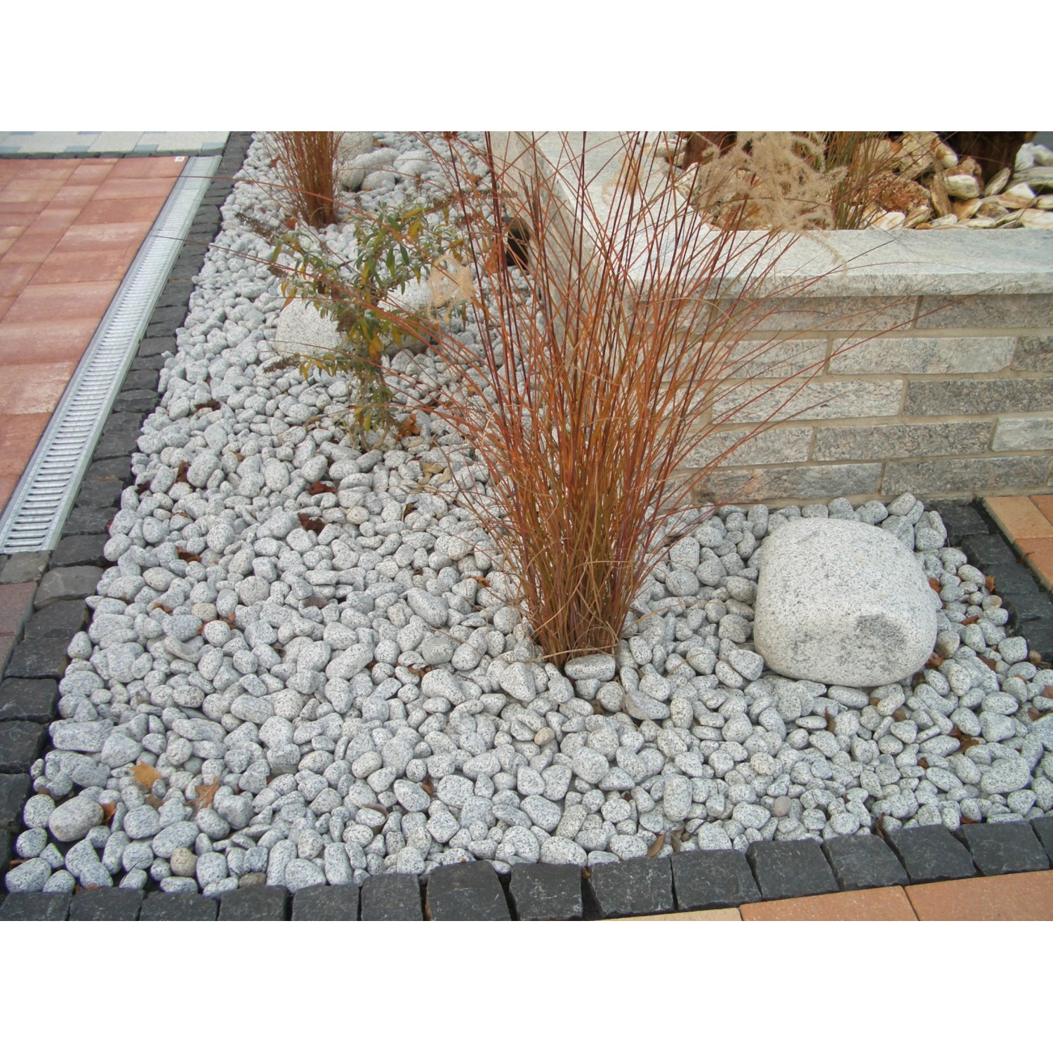 Beet mit Granitkies Gletscher Grau (30-60mm) als Zierkies, mit Pflanzen dekoriert.