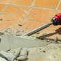Einhell Bohr-Meissel-Set im Einsatz: Spitzmeißel zertrümmert Fliese mit rotem Bohrhammer. Ideal für Abbrucharbeiten.