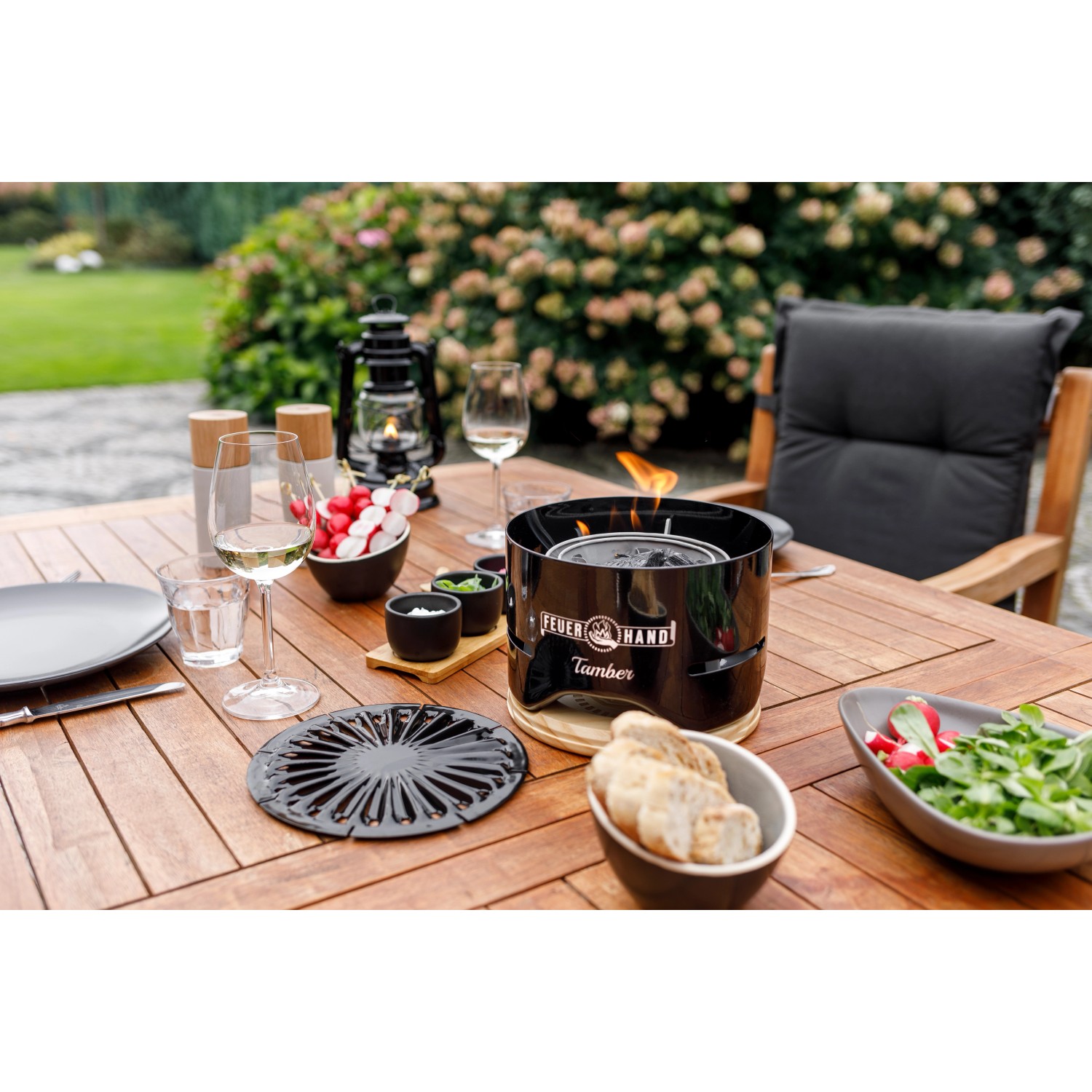 Feuerhand Tischgrill Tamber, tiefschwarz, mit Grillrost und Zubehör auf einem Gartentisch.
