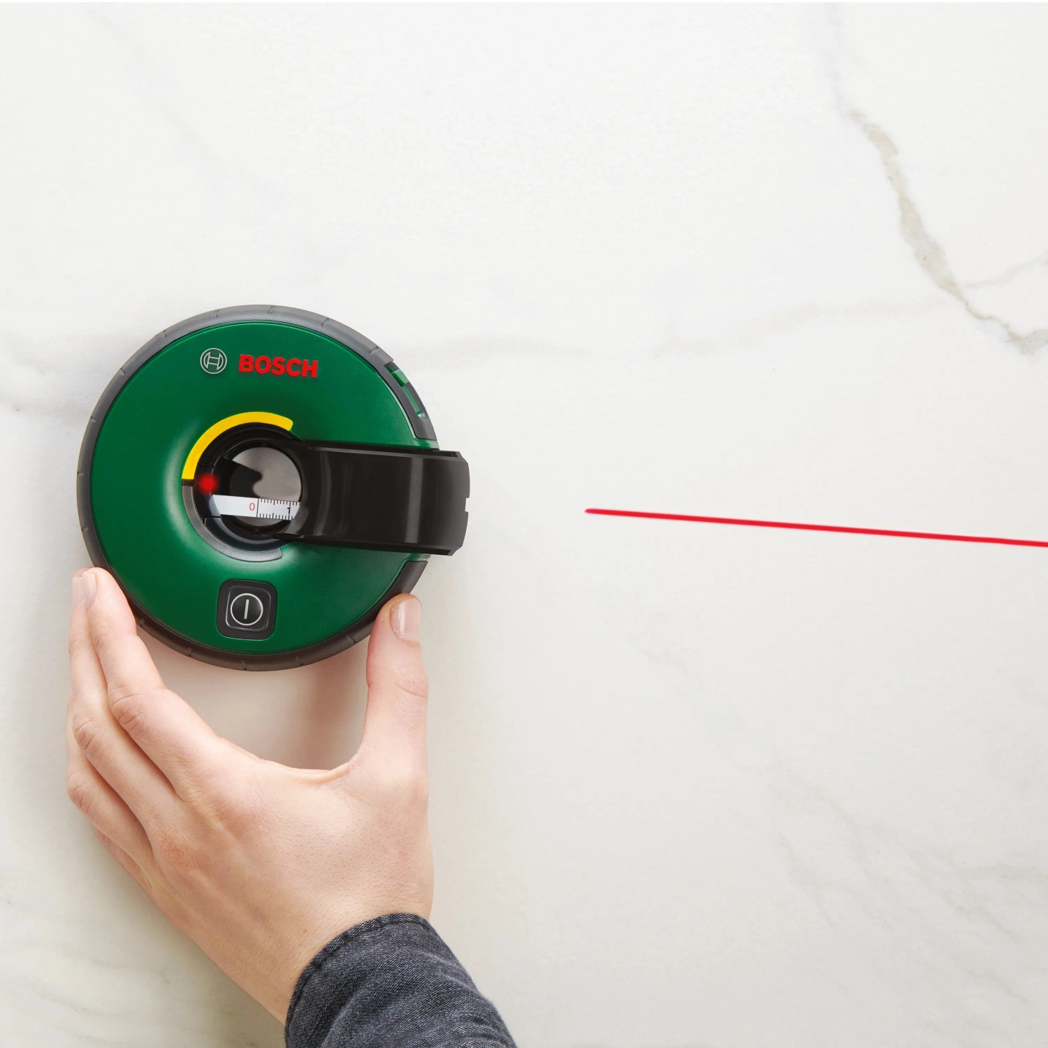Bosch Atino Linienlaser mit roter Laserlinie an Wand, gehalten von Hand. Prüfwerkzeug zum Ausrichten.