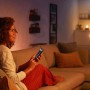 Frau steuert Philips Hue Filament Lampe E27 mit dem Smartphone im Wohnzimmer.