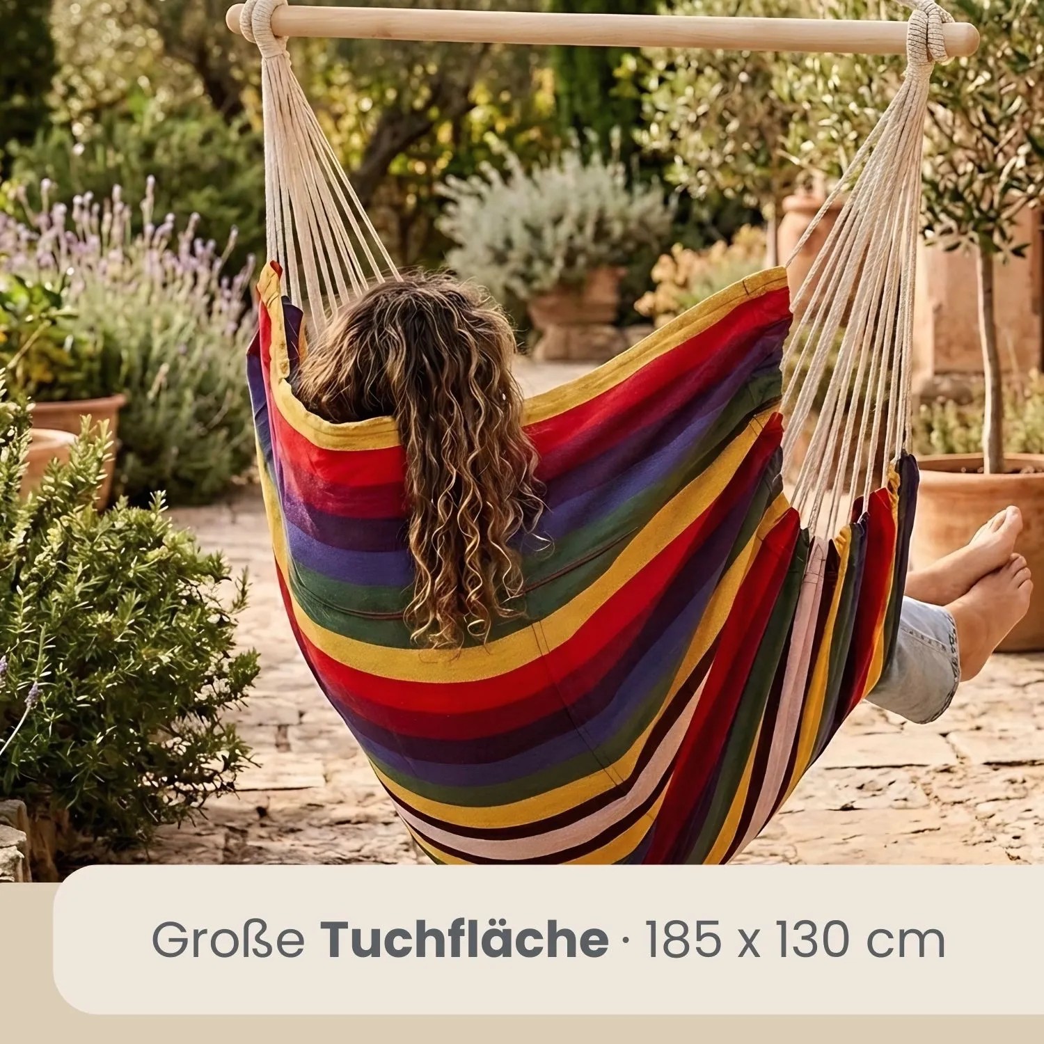 Person entspannt im bunten AMANKA Hängesessel (185x130 cm) mit Holzstab im Garten. Regenbogenfarben.