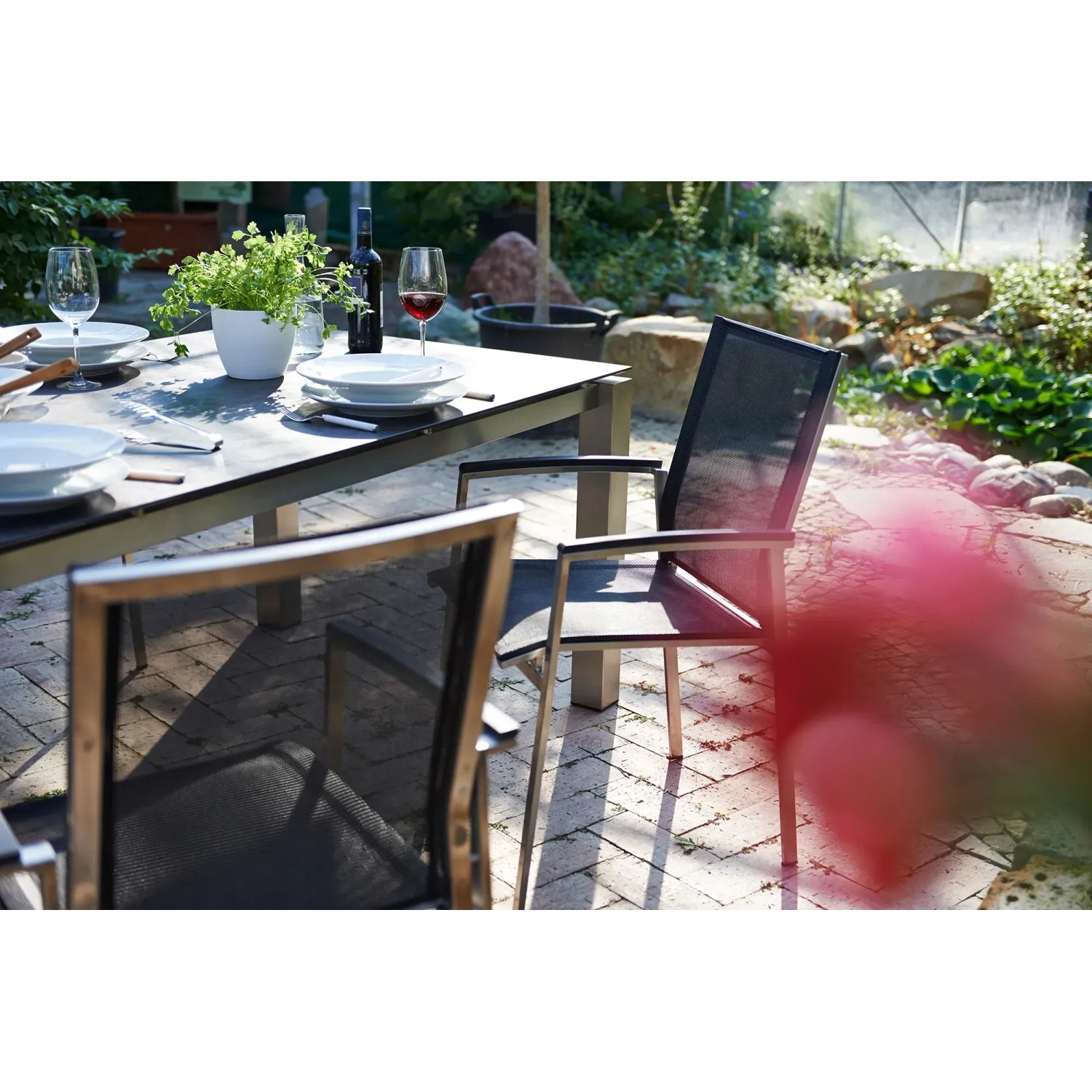 Acamp Gartenmöbel-Set Auris mit Esstisch und Stapelsesseln aus Edelstahl und dunklem Textilbezug.